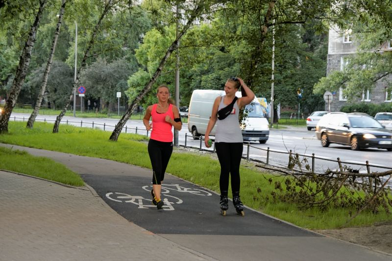 Huebsche Joggerin und huebsche Rollerskaterin nehmen den Radweg in Beschlag
